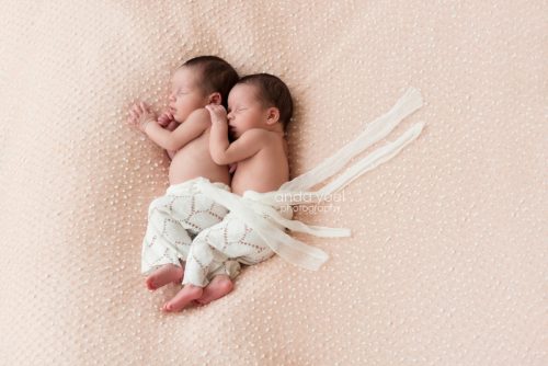 אחיות תינוקות תאומות עם מכנס לבן אחת ליד השנייה על רקע בד ורוד עם נקודות לבנות - מסדרת צילומי ניובורן תאומים, אנדה יואל